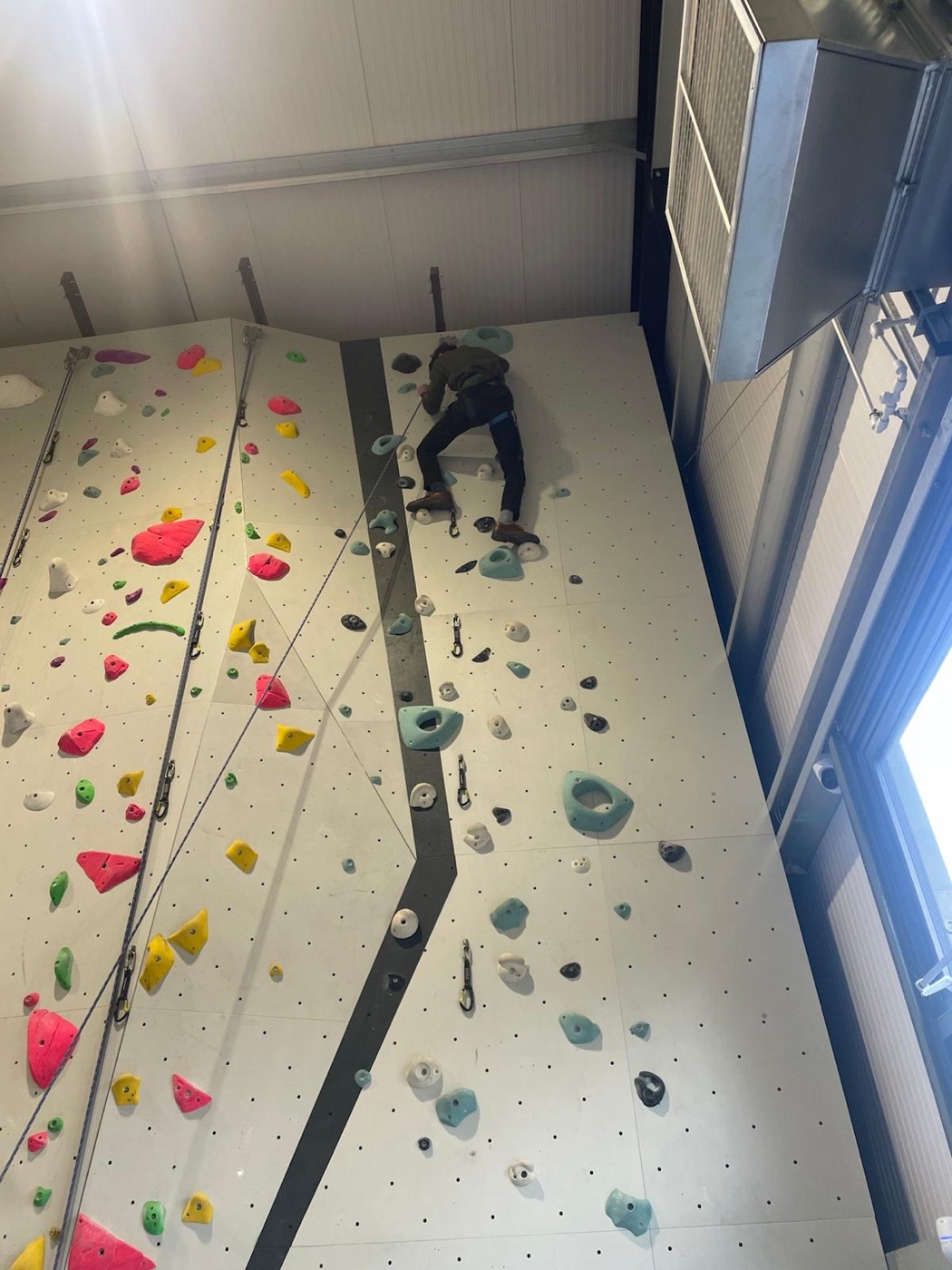 A client climbing an indoor climbing wall on a rope during a community rehabilitation session